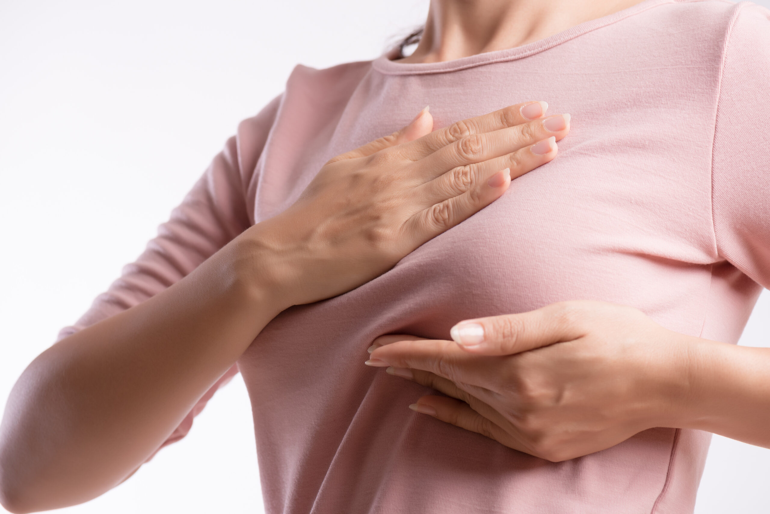 Woman hand checking lumps on her breast for signs of breast cancer on gray background. Healthcare concept.